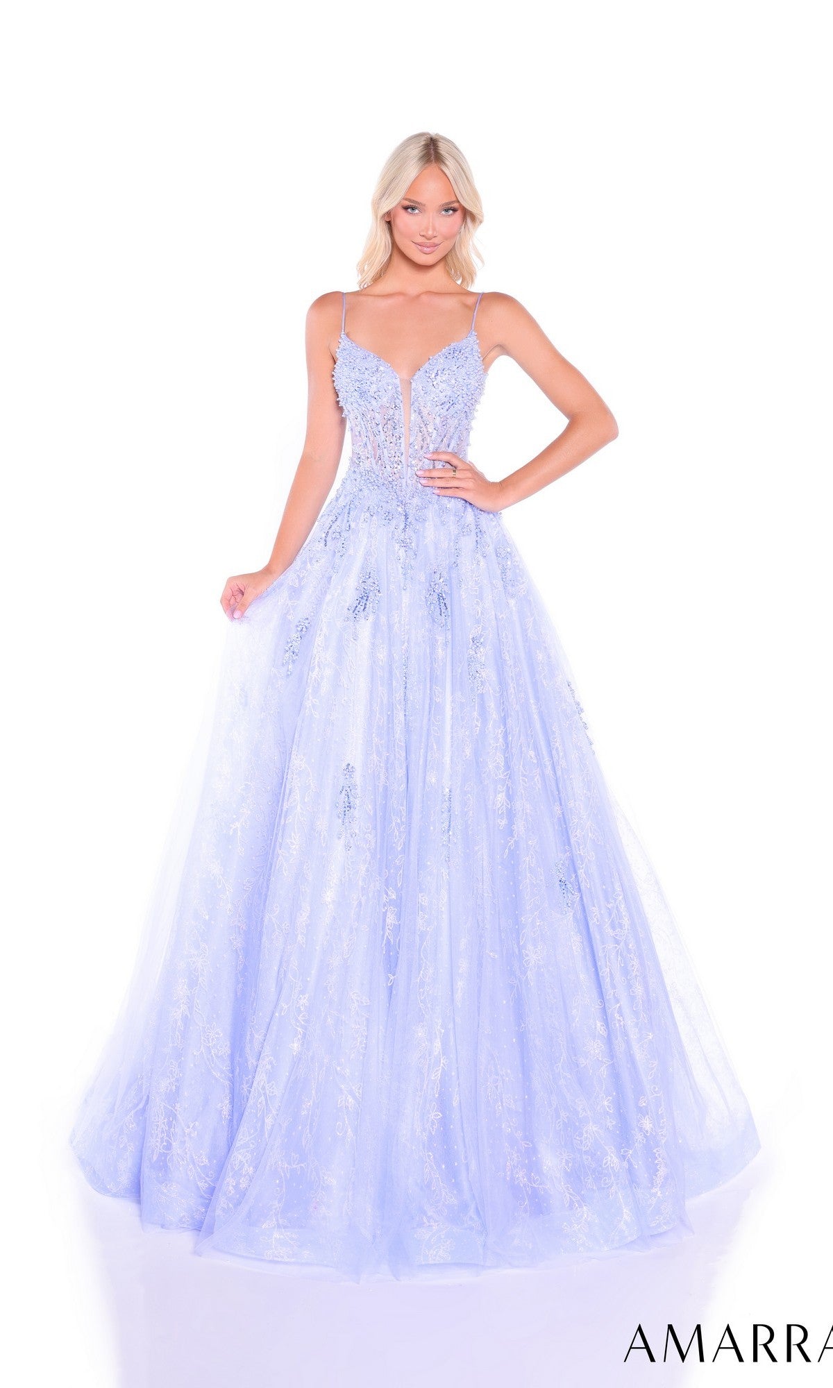 A woman stands against a white background wearing the Amarra 89425, a light blue, floor-length glitter tulle prom dress featuring thin straps, a deep neckline, and delicate beaded appliques.